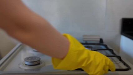 Person in yellow gloves removes stove grates from four-burner cooktop and prepares to spray cleaner, realistic household cleaning and hygiene concept.  - Powered by Adobe