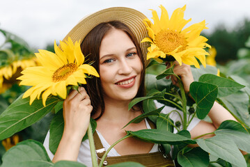 young beautiful brunette caucasian woman on farm in sunflower field in summer day, smiling widely, eco style clothes, green dress, straw hat