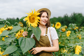 young beautiful brunette caucasian woman on farm in sunflower field in summer day, smiling widely, eco style clothes, green dress, straw hat