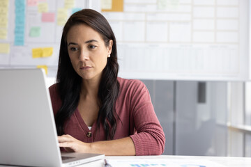 Serious Latina businesswoman working on laptop seated at workplace desk