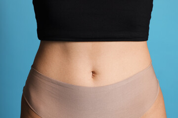 Young woman with flat belly on light blue background, closeup