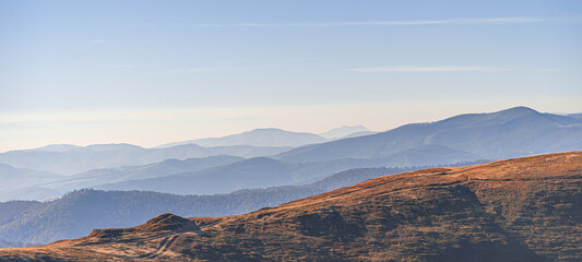 A panoramic view of layered mountain ridges bathed in soft light, creating a serene and tranquil natural landscape.
