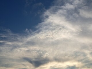 Evening sunset with a yellow blue sky – White and grey clouds illuminated by the last remaining rays of the bright yellow evening sun, amidst a darkening blue sky.
