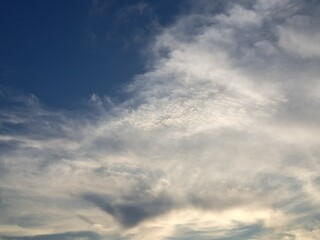 Evening sunset with a yellow blue sky – White and grey clouds illuminated by the last remaining rays of the bright yellow evening sun, amidst a darkening blue sky.