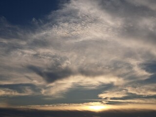 Evening sunset with a yellow blue sky – White and grey clouds illuminated by the last remaining rays of the bright yellow evening sun, amidst a darkening blue sky.
