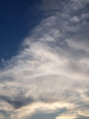 Fototapeta premium Evening sunset with a yellow blue sky – White and grey clouds illuminated by the last remaining rays of the bright yellow evening sun, amidst a darkening blue sky.