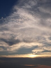 Evening sunset with a yellow blue sky – White and grey clouds illuminated by the last remaining rays of the bright yellow evening sun, amidst a darkening blue sky.