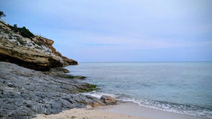 Scenic seashore with rocky cliffs on the left, sandy foreground and sea on the right. Beautiful coastal landscape on a sunny day.
