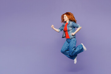 Full body side view young ginger woman she wearing red t-shirt denim shirt jump high run fast hurry up be in rush isolated on plain pastel light purple background studio portrait. Lifestyle concept.