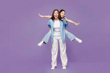 Obraz premium Full body young woman child baby girl 8-9 years old wear blue clothes. Mommy little kid daughter give piggyback ride to joyful, sit on back isolated on plain purple background. Mother's Day concept.