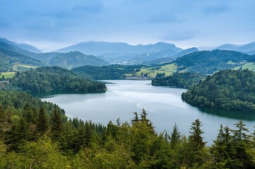 Tranquil lake nestled among lush green hills and foggy mountain ranges, presenting a calm and scenic natural retreat.