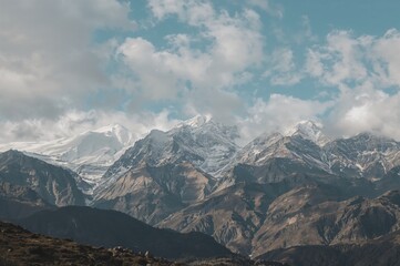Fototapeta premium Vertical shot of a snow-covered mountain range with peaks obscured by clouds in the distance, showcasing a majestic alpine landscape.