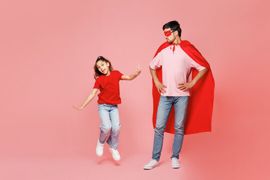 Full body young fun parent man child girl wearing red casual clothes super hero coat mask Daddy little kid daughter jump high isolated on plain pastel pink background Father's Day Love family concept - Powered by Adobe