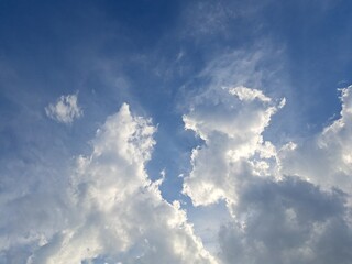 Obraz premium Late afternoon sun illuminating the clouds in the blue sky – White and grey clouds illuminated by the strong rays of the late afternoon sun, amidst a blue sky.