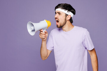 Young sad mad strong fitness trainer instructor man sportsman he wear headband t-shirt train in home gym scream shout in megaphone isolated on plain purple background. Workout sport fit abs concept.