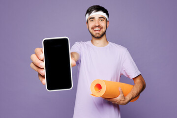 Young fitness trainer instructor sporty man wear headband t-shirt train in home gym hold yoga mat...