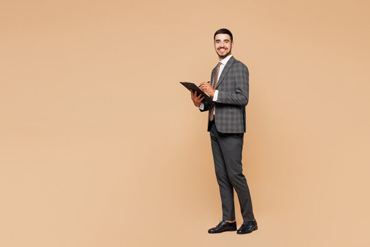 Fototapeta Full body young successful employee business man corporate lawyer wear classic formal grey suit shirt tie work in office hold clipboard with paper account documents isolated on plain beige background.