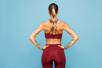 Back rear view young slim skinny fitness trainer instructor sporty woman sportsman wears red sportswear train in home gym look aside isolated on plain blue background. Workout sport fit abs concept.