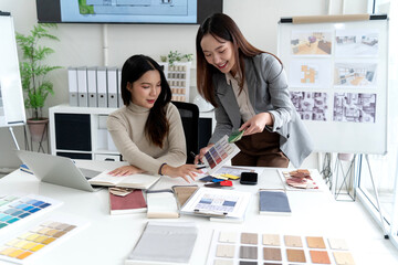 Asian adult women interior designers project planning selecting material samples color palettes modern office workspace design studio.