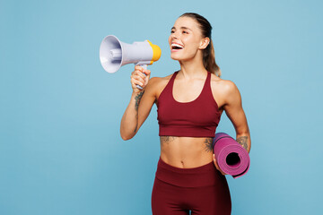 Young fitness trainer instructor woman sportsman wear red sportswear train in home gym hold yoga mat scream in megaphone about sales isolated on plain blue background. Workout sport fit abs concept.
