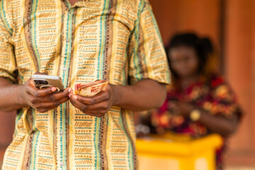 Mobile money (MoMo), customer counts cash after withdrawal transaction at an outdoor stand. Fintech, digital payments and financial inclusion in Africa. © Roger