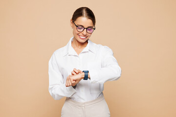 Young happy successful employee business woman corporate lawyer in classic formal white shirt glasses work in office look at smart watch check time isolated on plain beige background studio portrait