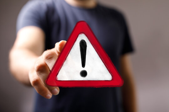 Hand of a person presenting or holding a digital red triangular warning sign with an exclamation mark. Concept of danger, alert, error, or cauti