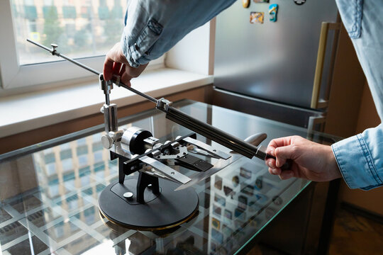 Manual High Precision Guided Sharpening Equipment for knives. A man sharpens a chef's knife with a sharpening system in the kitchen.