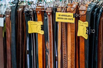 Handmade leather belts displayed for sale at a street market stall, with visible price tags and a sign offering free size adjustments for customers