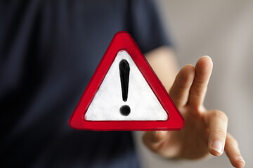 A human hand interacts with a glowing digital warning sign, emphasizing concepts of danger, alert, error, and caution in a modern technological