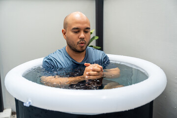 Man practices cold therapy and ice bathing in inflatable tub, using Wim Hof Method for wellness,...
