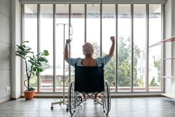 A male cancer patient in a wheelchair with an IV smiles with joy and hope showing strength and...