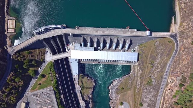 Aerial drone descends above Roxburgh hydro dam, unveiling the power station, reservoir waters, and scenic Central Otago surroundings in New Zealand.