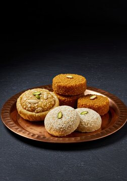 Traditional Indian Sweets: Ghevar, Motichoor Ladoo, and Petha on a Copper Platter with Dark Background