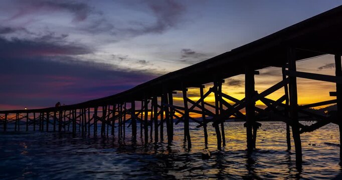 Stunning time lapse video of a mesmerizing sunset over a tranquil ocean, with a wooden pier stretching into the calm waters in the foreground. The sky transforms into vibrant hues of orange and red
