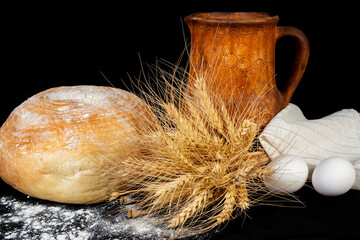Freshly baked bread with wheat, eggs, and a rustic clay mug on a dark background