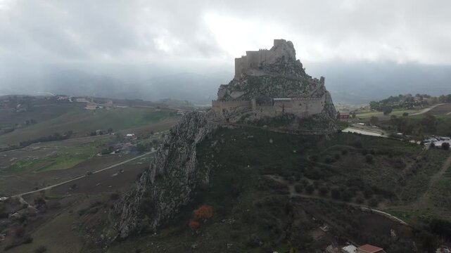 Aerial 4k drone footage of Mussomeli Castle in Sicily, Italy, featuring the historic fortress, dramatic misty atmosphere, surrounding hills, and panoramic views of the landscape