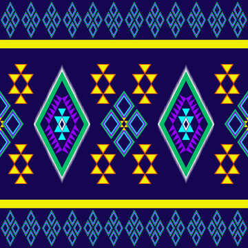 Traditional seamless tribal geometric pattern with colorful diamond and triangle motifs in purple, green, yellow, and orange on a dark navy background. Perfect for textile, fabric, wallpaper, and digi