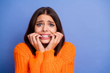 Young woman in orange sweater with nervous expression on blue background, showing playful emotions - ideal for lifestyle and fashion content