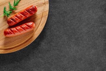 two grilled sausages and herbs on dark countertop, top view