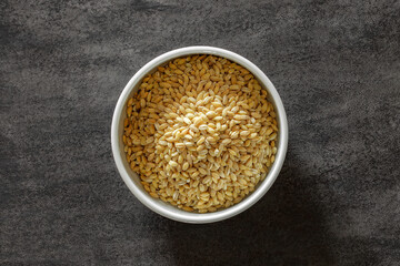 raw wheat groats in bowl on dark countertop, top view