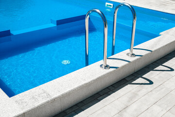 stairs with metal handrails in swimming pool with blue water