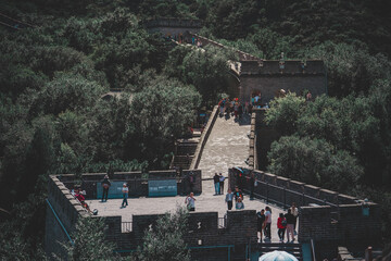 Ancient stone fortifications snake across a mountainous landscape, showcasing a historic Beijing landmark with tourists exploring its rough, textured surface under a clear, sunny day.