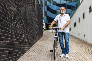 Happy senior man walks his bicycle outdoors and smiles. Cheerful old healthy man enjoy a peaceful walk with bike in a urban scene. Elderly man in casual outfit strolls through the city with bicycle.