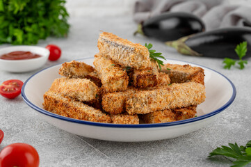 Baked crispy eggplant sticks served with tomatoes sauce on a plate on a gray concrete background. Vegetarian healthy dish. Selective focus