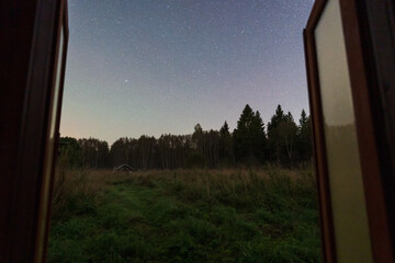 Obraz premium A tranquil view from an open door, overlooking a grassy field and the starry night sky in rural Estonia.