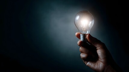 A hand holds a glowing light bulb symbolizing a bright idea and innovation against a dark smoky background
