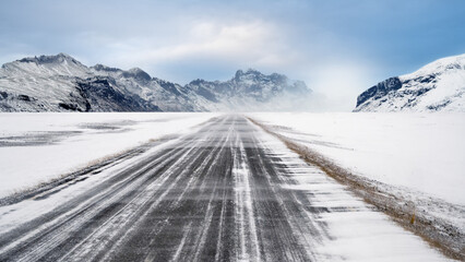 View of a long road stretches towards the snow-covered mountain under a bright blue sky on a winter day. Beautiful landscape for a natural or winter background or wallpaper