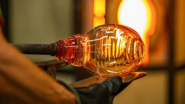 Close-up of molten glass being shaped by a craftsman during the glassblowing process, glowing orange from the intense heat of the furnace, with intricate reflections on the glass surface