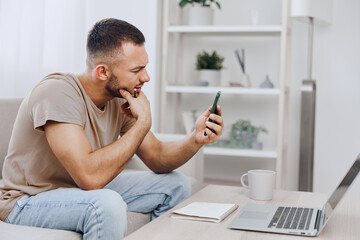 Thoughtful man using smartphone while sitting on sofa, engaged in work, casual attire, modern interior design, creating a focused atmosphere.